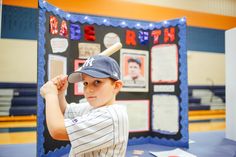 a young boy holding a baseball bat in front of a poster with pictures on it