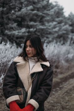 a woman standing in the grass with her hands on her hips wearing red mittens