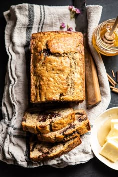 sliced loaf of banana bread next to butter and honey on a towel with spoons