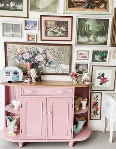 a pink cabinet sitting in front of a wall filled with pictures and vases on top of