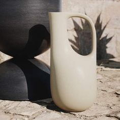 a white vase sitting on top of a stone floor next to a large black object