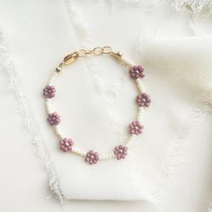 a bracelet with pink flowers and pearls is on a piece of white cloth next to a gold chain