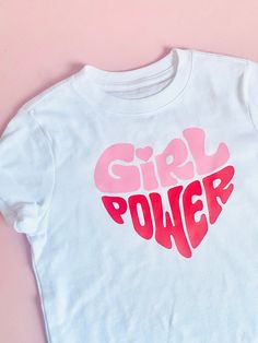 Graphics Tees / Girls & Adult  Front Design: Girl Power Back: Blank  Details:  - Gildan Tshirt - Soft Cotton    (100% Cotton), short sleeve.  - Front Design: Red & Pink Vinyl  - T-shirt colors available:      * Black     * White  * The sizing of the design will be proportional to the size of the t-shirt * Available sizes: * Toddler & Youth  - 2T - 3T - 4T - 5T - 6 - 8 - 10 - 12 * Teen's & Adult  - XSmall  - Small  - Medium  - Large - XLarge  - XXLarge Super comfortable, soft and fashionable. Playful Pink T-shirt With Slogan, Playful Letter Print T-shirt, Playful Pink T-shirt With Text Print, White Playful T-shirt With Heart Graphic, Playful White T-shirt With Heart Graphic, Playful Pink Text Print T-shirt, Trendy Pink T-shirt With Heart Graphic, Cute Short Sleeve Tops With Graphic Design, Playful Pink T-shirt With Screen Print