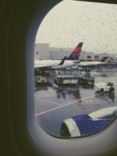 an airplane window with rain drops on the glass and airplanes parked at the airport in the background