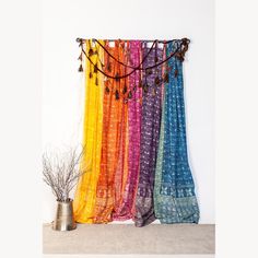 multicolored scarfs hanging on the wall next to a potted plant and vase