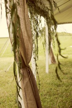 an outdoor wedding ceremony with greenery and burlock draped over the top of the tent