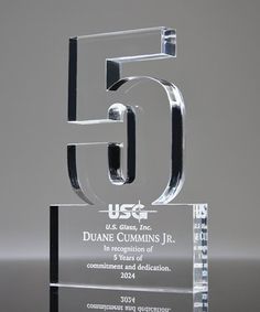 a clear glass award with the letter g in it's center, on a reflective surface