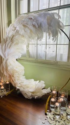 an arrangement of candles and feathers in front of a window