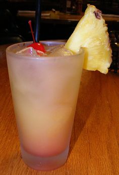 a pineapple drink with a cherry garnish on the rim is sitting on a wooden table