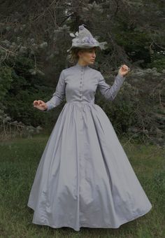 This Halloween, experience the allure of wearing this grey cotton dress - a true Victorian cut. From the tailored fit of the straight cut bodice to the modest high collar neckline and long tapered set sleeves, this dress is perfect! The graceful four-paneled skirt is full enough to accommodate a hoop or petticoat. Front button closure with metal button accents. What a delightful dress! Hand wash or machine wash gently. Tumble dry. 100% cotton. Liesa is wearing an extra full crinoline, grey witch 1880 Dress, Grey Cotton Dress, Victorian Dress Gown, Grey Witch, Hedda Gabler, Fashion Eras, Victorian Era Dresses, Making A Wedding Dress, Victorian Elegance