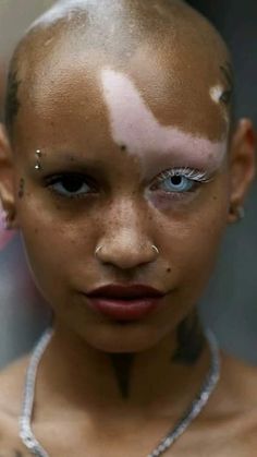 a woman with white makeup and piercings on her face is looking at the camera