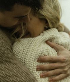 a man and woman hugging each other while wearing sweaters