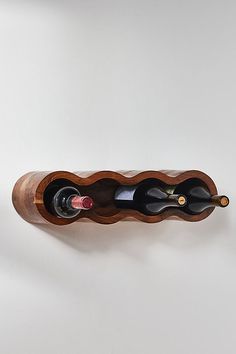 a wooden wine rack with three bottles of wine in it on a white wall background