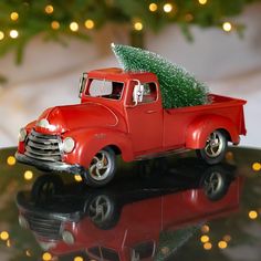 an old red truck with a christmas tree on the back is sitting on a table