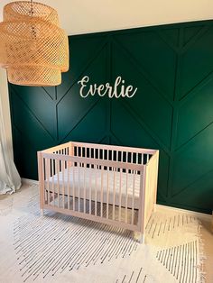 a baby crib in front of a green wall with the name everlie written on it