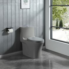 a white toilet sitting next to a window in a room with gray walls and tile flooring