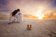 two people sitting in the sand with their backs to each other as the sun sets