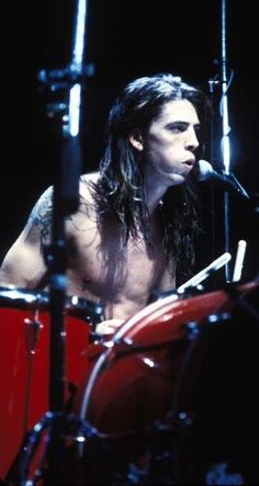 a man with long hair and no shirt playing drums in front of a drum set