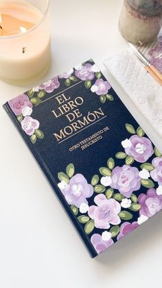 a book sitting on top of a white table next to a candle and some flowers