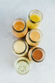 five jars filled with different colored liquids on a white surface, next to each other