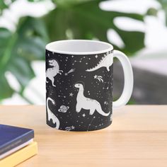 a black and white mug with dinosaurs on it sitting on a table next to books