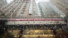 a train traveling down tracks next to tall buildings in the rain with lots of windows