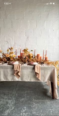 a long table with candles and flowers on it is set against a white brick wall