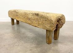 a wooden bench made out of logs in a room with concrete flooring and white walls