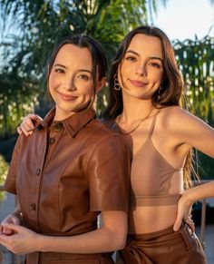 two beautiful young women standing next to each other in front of a palm tree with their arms around each other