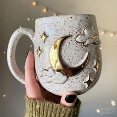 a hand holding a coffee cup with the moon and stars painted on it