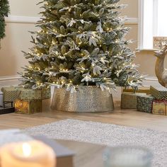 a decorated christmas tree in a living room with presents around it and a lit candle on the floor