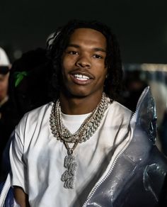 a young man with long hair wearing a white t - shirt and silver necklaces