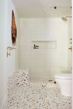 a white toilet sitting in a bathroom next to a walk in shower and tiled walls