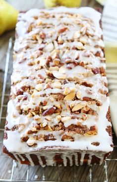 a loaf of cake with nuts and icing on a cooling rack next to bananas