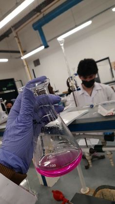 a person in a lab coat and purple gloves holding a flask filled with liquid