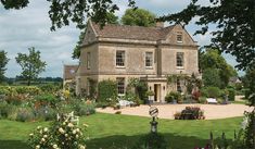 a large house surrounded by lush green trees and flowers in front of it is a garden