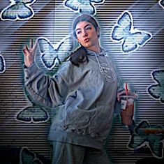 a woman standing in front of a wall with butterflies on it and holding a drink