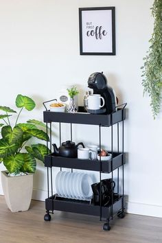 a black shelf with plates and cups on it next to a potted green plant