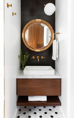 a bathroom with black and white tile flooring and a round mirror above the sink