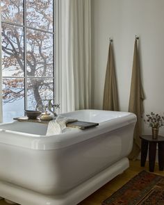 a white bath tub sitting in front of a window next to a rug and table