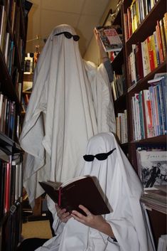 a person dressed as a ghost reading a book in front of a bookshelf