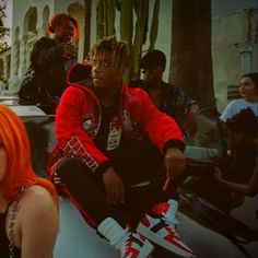 two people sitting on the hood of a car in front of cactus trees and one person with orange hair