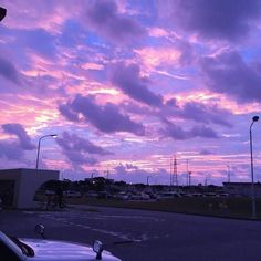 the sky is purple and pink as it sets over a parking lot with parked cars