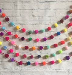 multicolored pom - pom garland hanging on a brick wall