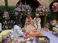 two people sitting on the ground in front of some flowers and plates with food around them