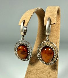 Elevate your style with our Handmade Earrings featuring spectacular orange amber set in textured 925 sterling silver. These exquisite earrings are designed for women who appreciate unique and original jewelry. The vibrant orange amber stones are beautifully complemented by the textured silver, creating a stunning and eye-catching piece that adds a touch of elegance and sophistication to any outfit. Product Details: Material: 925 Sterling Silver Stone: Orange Design: Textured Silver with Unique S Orange Oval Sterling Silver Jewelry, Classic Amber Sterling Silver Earrings, Silver Baltic Amber Earrings, Elegant Amber Sterling Silver Earrings, Vintage Amber Dangle Earrings, Vintage Amber Nickel-free Earrings, Orange Pierced Earrings For Formal Occasions, Formal Orange Pierced Earrings, Classic Brown Jewelry With Matching Earrings