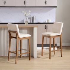 two white bar stools in front of a counter with flowers on the table and cabinets