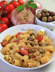 pasta with mushrooms, tomatoes and olives in a white bowl next to some garlic