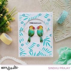 two green birds sitting on top of a card next to some flowers and other decorations