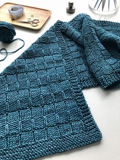 a blue knitted blanket sitting on top of a table next to yarn and scissors